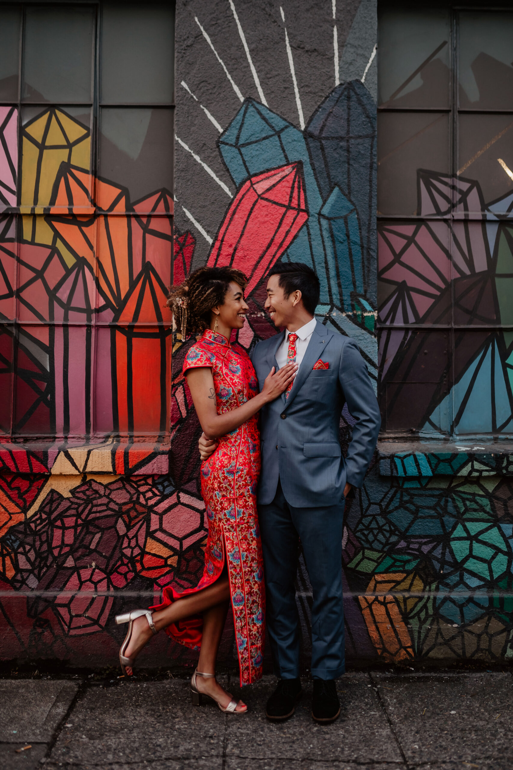 Woman and man looking at each other while standing in front of colorful wall in Capitol hill while dressed in Chinese wedding attire