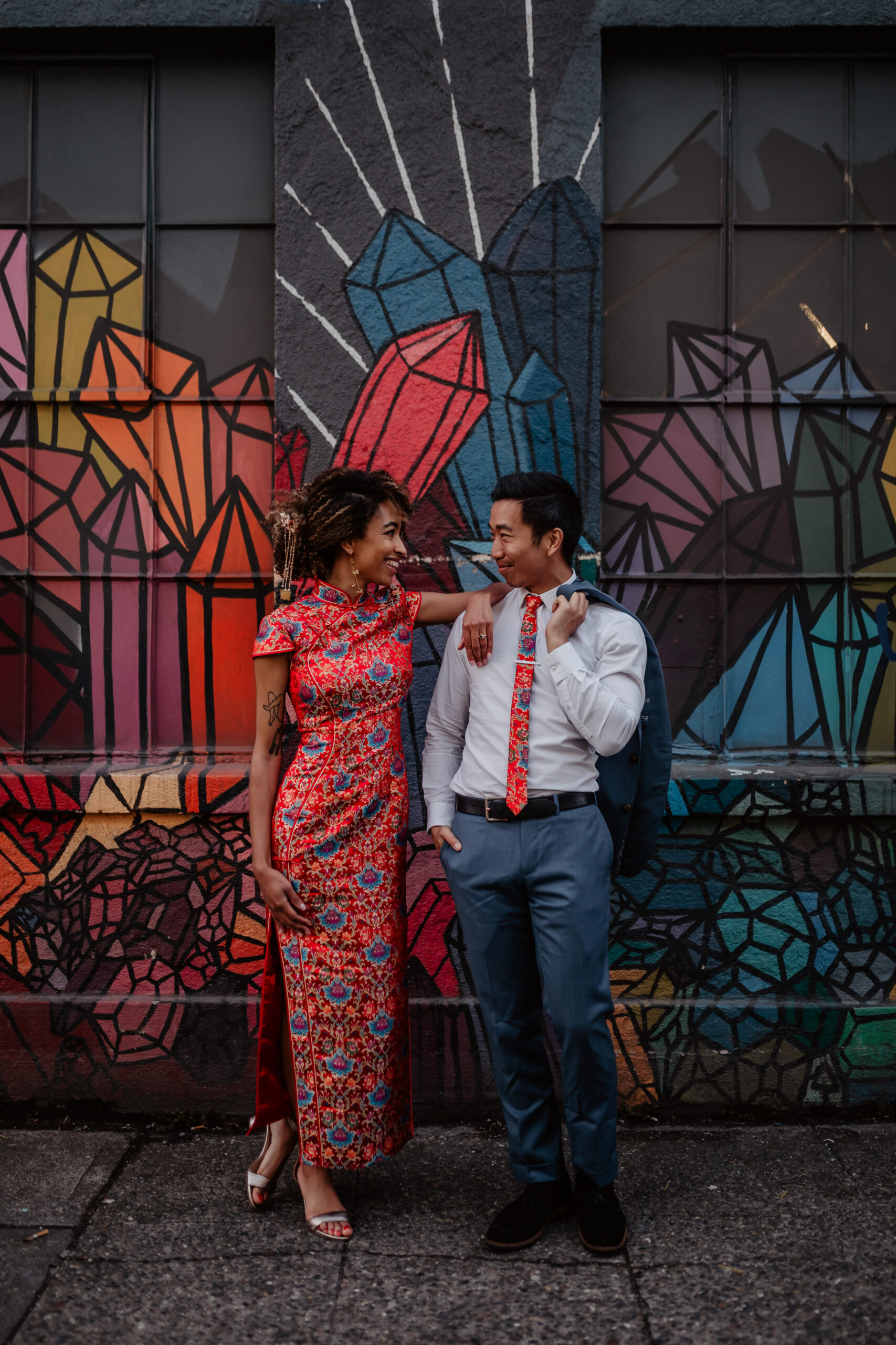 Woman in a red cheongsam leaning against a man in front of a colorful mural in Seattle
