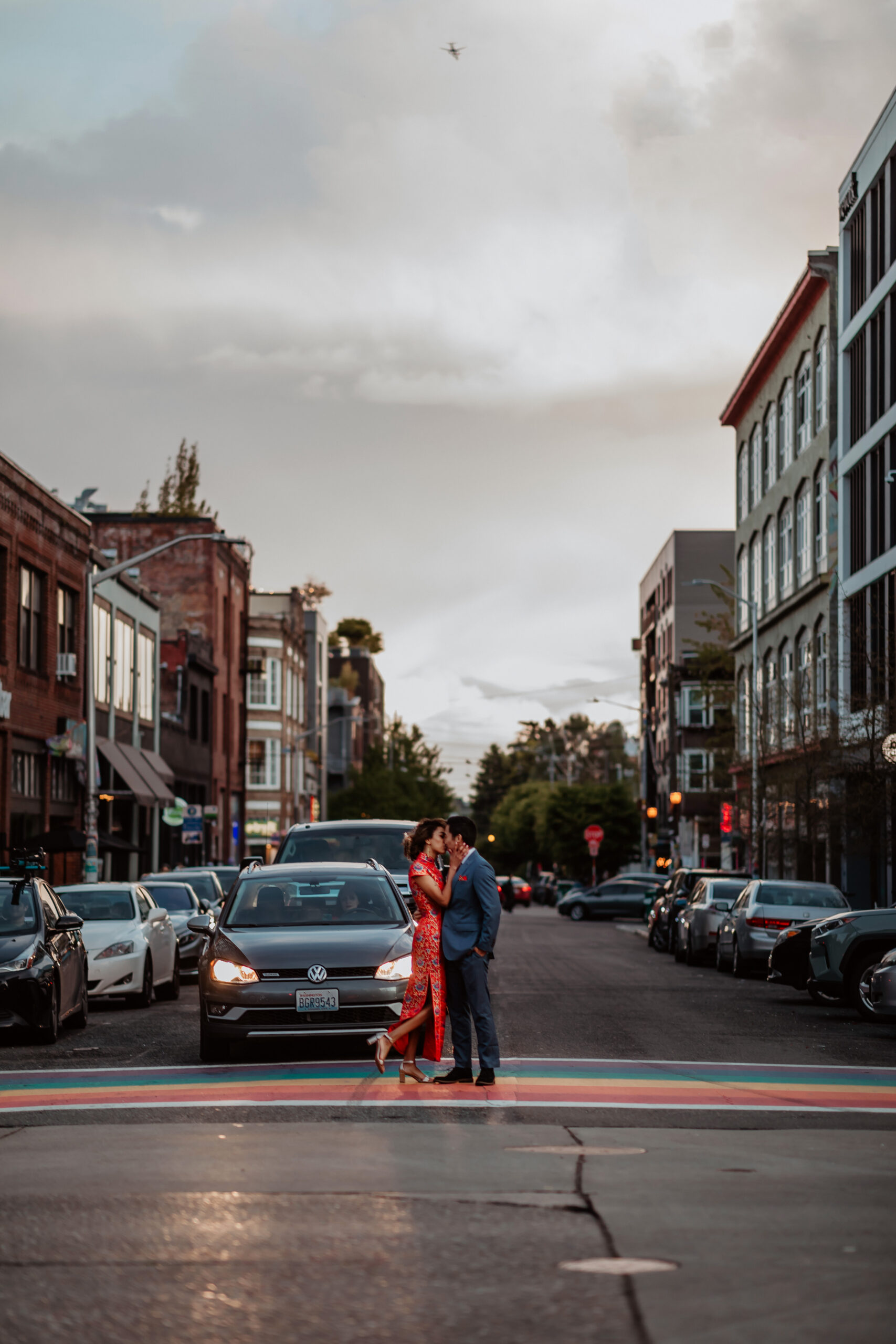 Couple wearing chinese wedding clothes kiss in rainbow crosswalk in Capitol Hill