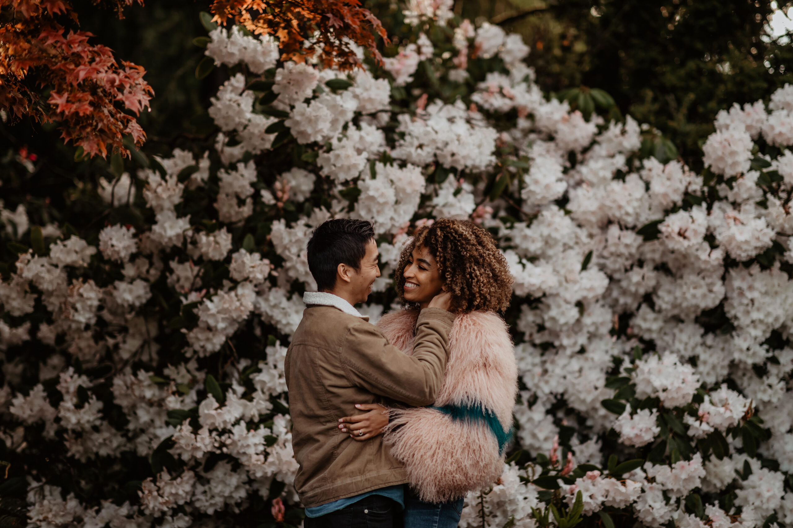 Couple embracing in front of floral bush.